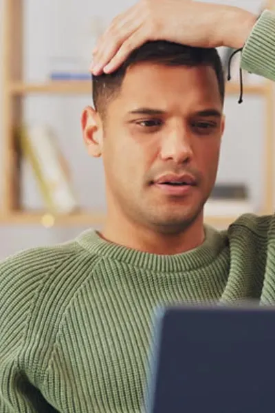 Frustrated man at a laptop with his hand on his head
